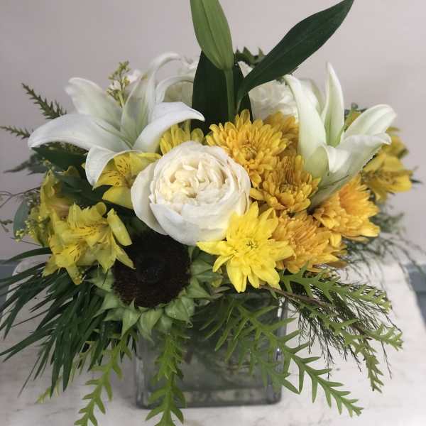 Yellow and white floral arrangement in a square glass vase