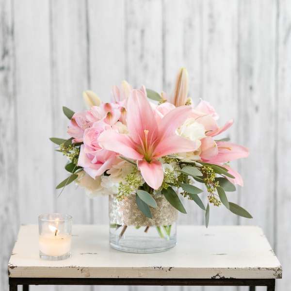 Pink lilies and roses in a glass vase beside a lit candle