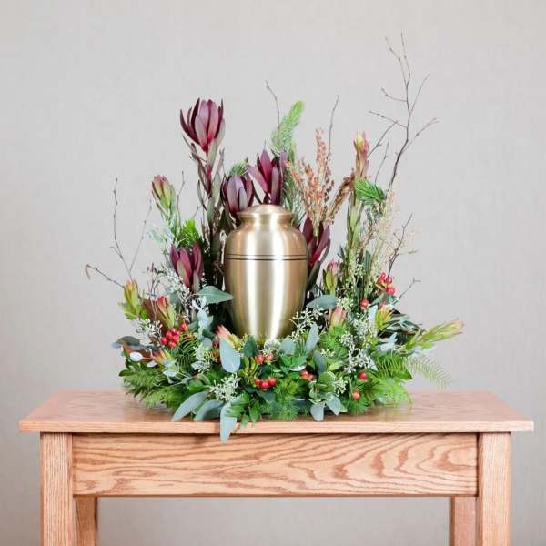 Floral urn arrangement with burgundy blooms and greenery around a gold urn