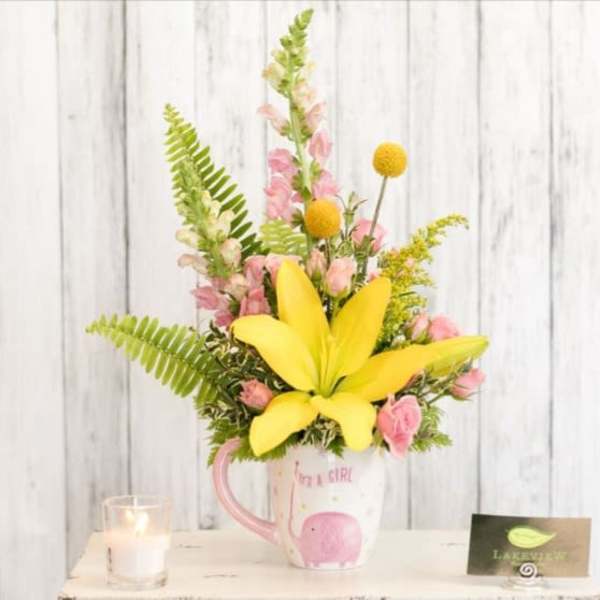 Yellow lily and pink flowers arranged in a mug with a baby girl design