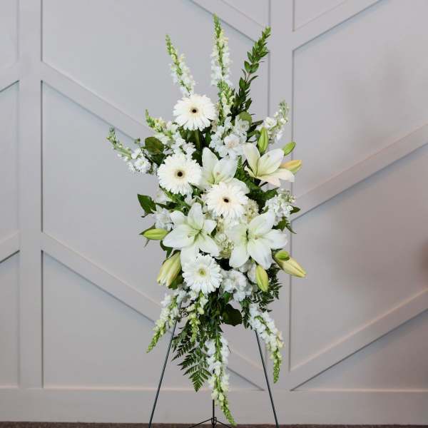 White floral standing spray on an easel with lilies and daisies