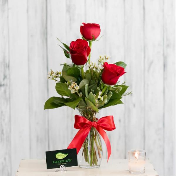 Three red roses in a clear vase with a red ribbon.