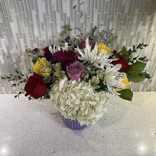 Mixed bouquet in a purple vase with roses, hydrangea, and white daisies