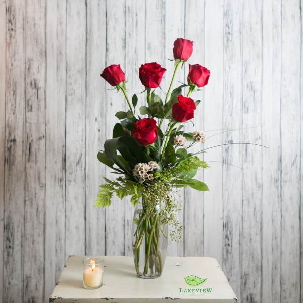 Red roses in a clear vase with a lit candle beside them