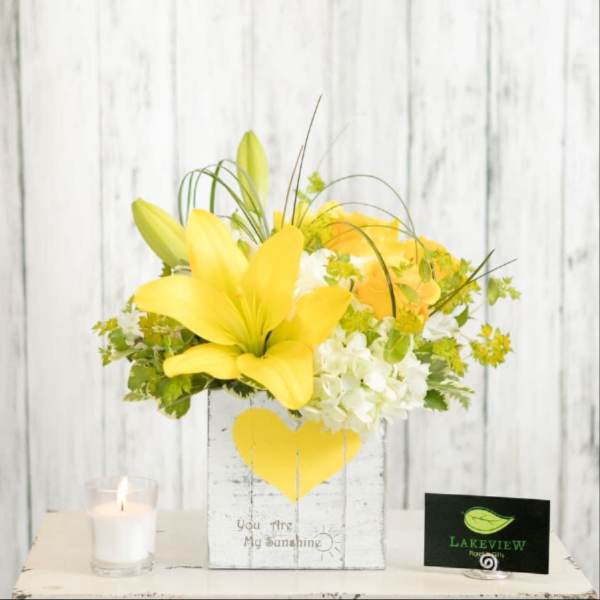 Yellow lily and white hydrangea arrangement in a heart-decorated box
