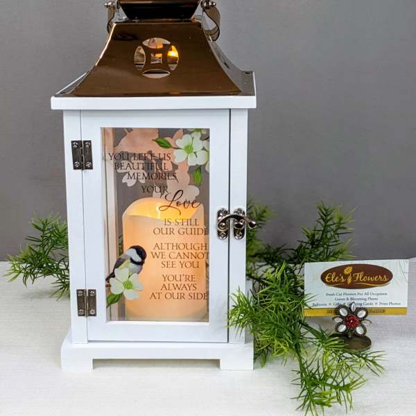 White memorial lantern with gold top and glowing candle, printed with verse and bird illustration.