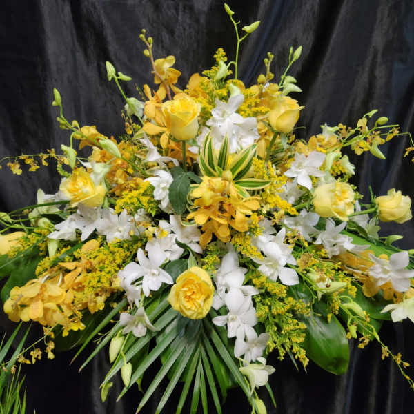 Yellow roses and white orchids arranged with greenery against a black background