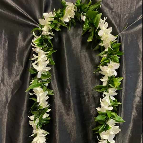 White floral lei with green leaves on dark fabric