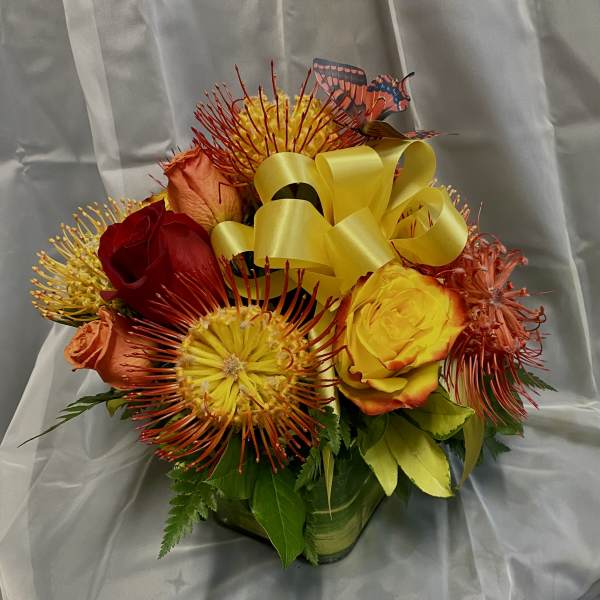 Bouquet of red, yellow, and orange roses with spiky blooms and a yellow ribbon
