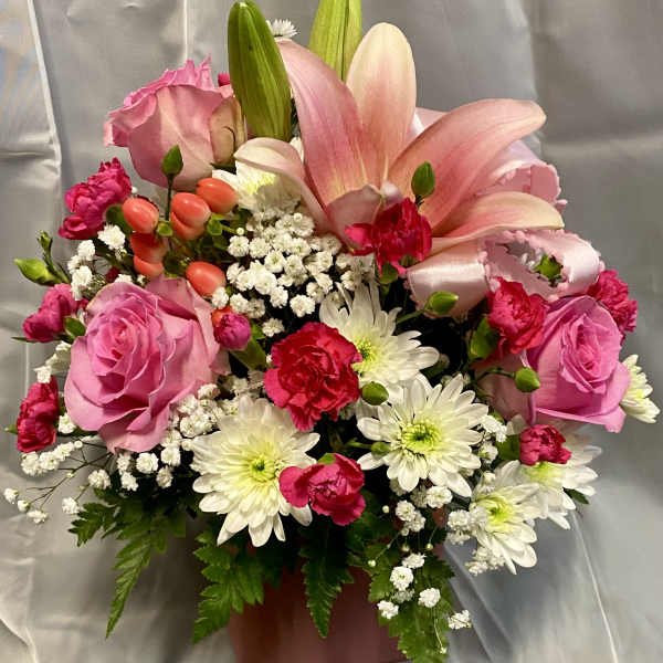Pink lilies and roses arranged in a vase with white daisies