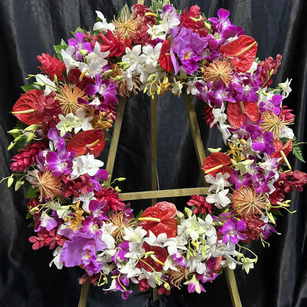 Large floral wreath with orchids, anthuriums, and red tropical blooms on a stand