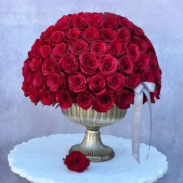 Red rose arrangement in a silver pedestal vase with a ribbon