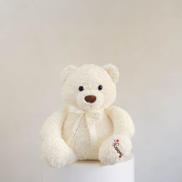 White teddy bear with a ribbon sitting on a pedestal