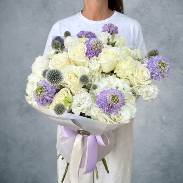 Large bouquet of white roses and lavender flowers wrapped in pale paper