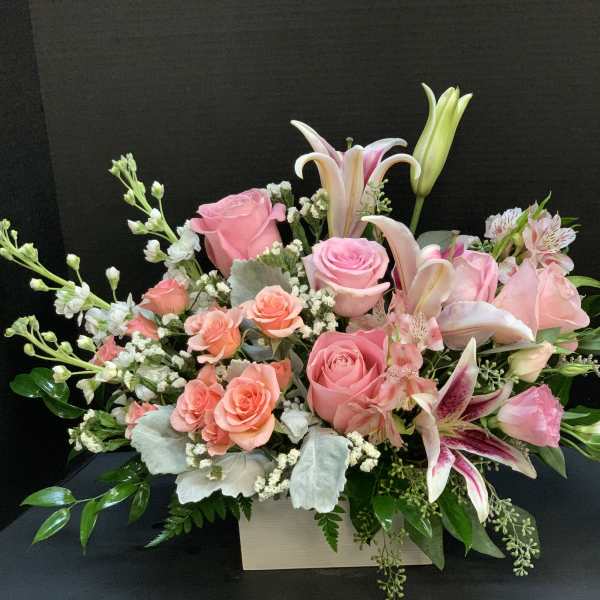 Pink roses and lilies arranged in a white box with greenery