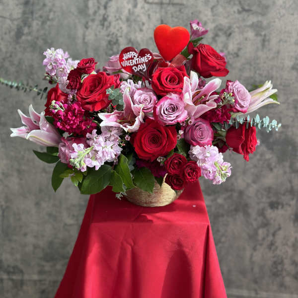 Red and pink rose bouquet with lilies and a heart topper in a basket