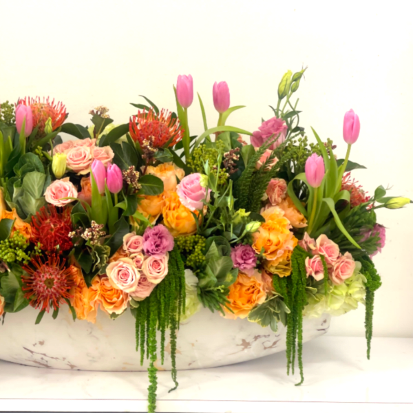 Large mixed floral arrangement with pink tulips and roses in a white bowl
