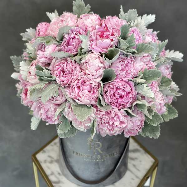 Pink peonies arranged in a gray hatbox with silvery foliage
