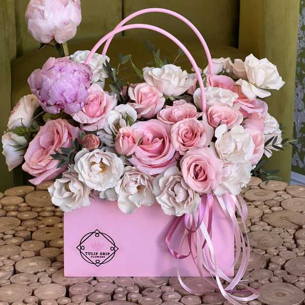 Pink and white roses arranged in a pink handled box with ribbon