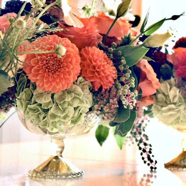 Two colorful floral arrangements in gold pedestal bowls