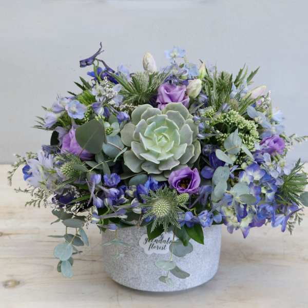 Lavender and blue floral arrangement with a succulent in a gray hatbox