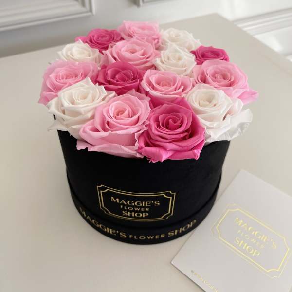 Pink and white roses arranged in a black round box