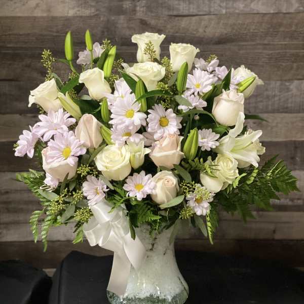White roses and pale daisies arranged in a glass vase with a ribbon