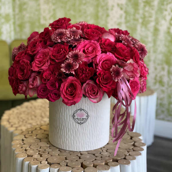 Pink and red rose arrangement in a white textured vase with ribbon