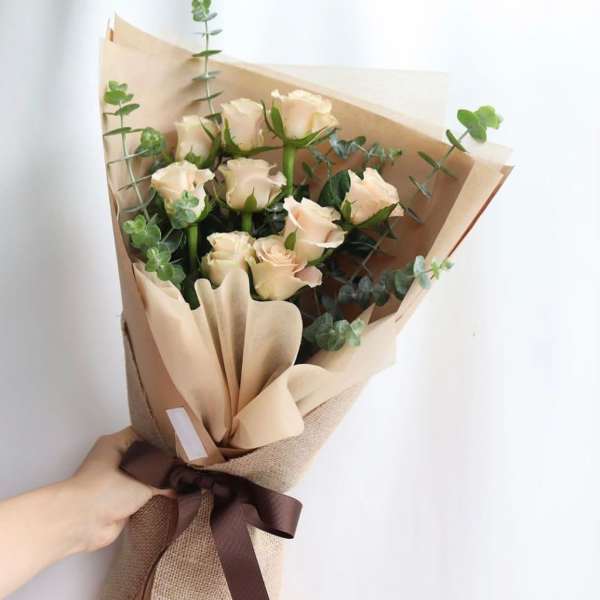 Bouquet of pale peach roses wrapped in brown paper with a ribbon