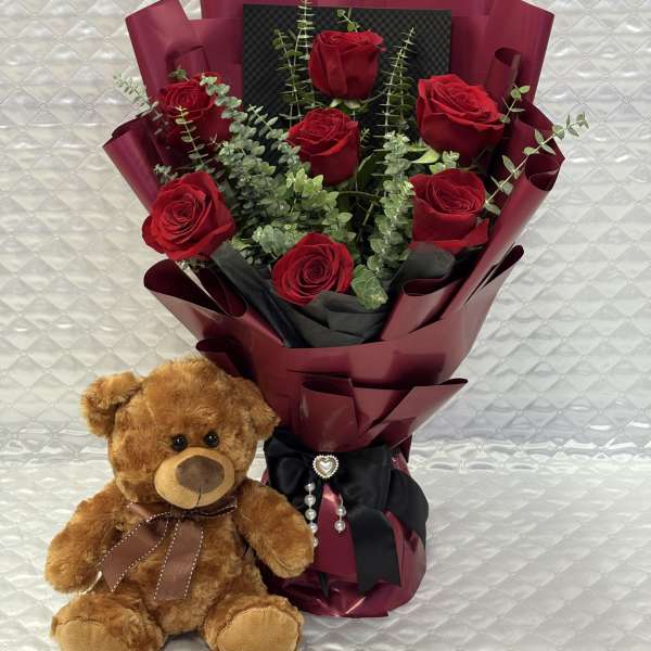 Bouquet of red roses with a teddy bear beside it
