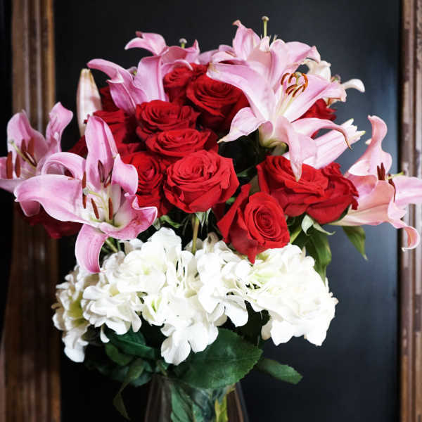 Bouquet of red roses, pink lilies, and white hydrangeas in a glass vase