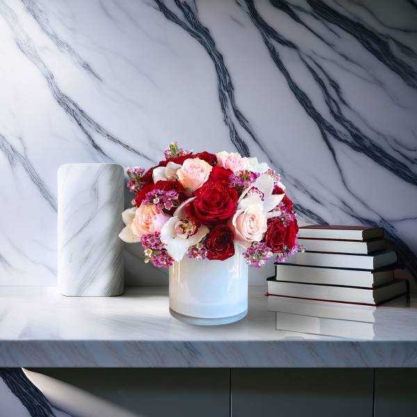 Red and blush roses arranged in a white vase beside stacked books