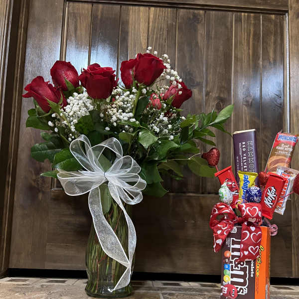 Red roses in a glass vase with a white ribbon and a candy gift box