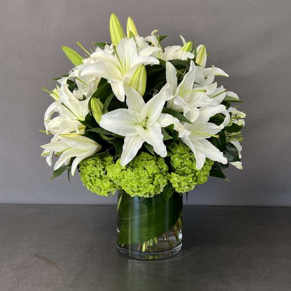 White lilies and green hydrangeas arranged in a glass vase