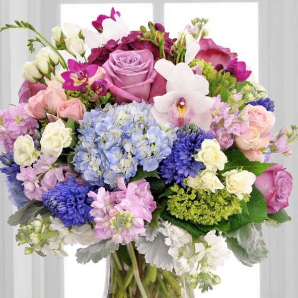 Mixed bouquet of pink, purple, blue, and white flowers in a clear glass vase