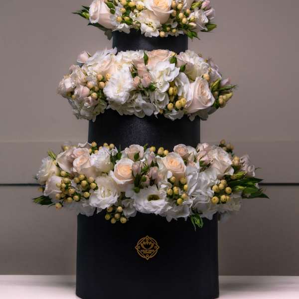 Three-tier floral arrangement of white and blush roses in a black box