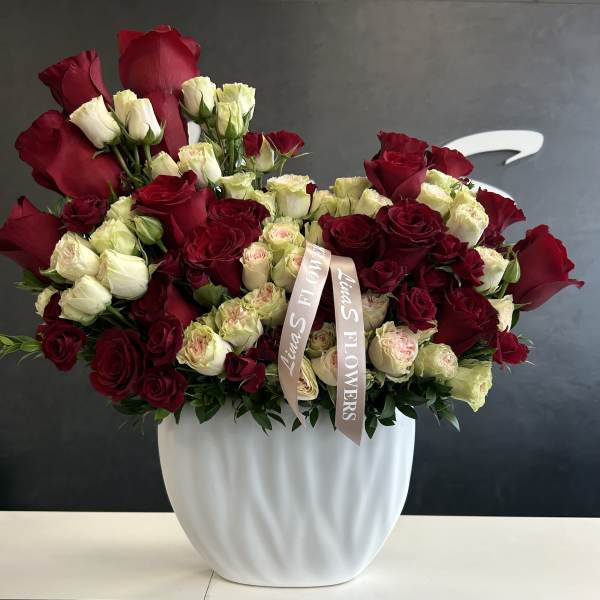 Red and cream rose arrangement in a white vase with a ribbon