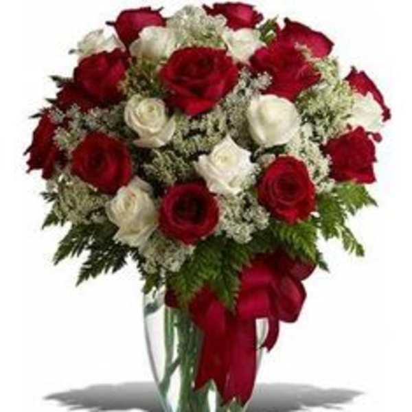 Red and white roses in a clear glass vase with a red ribbon