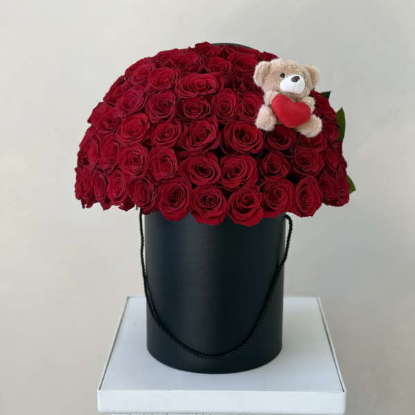 Red rose arrangement in a black hatbox with a small teddy bear holding a heart