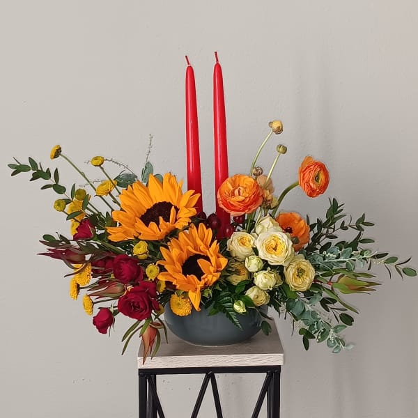 Colorful floral centerpiece with two red candles in a bowl vase