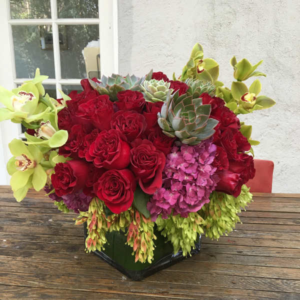 Red roses with green orchids and succulents in a black vase