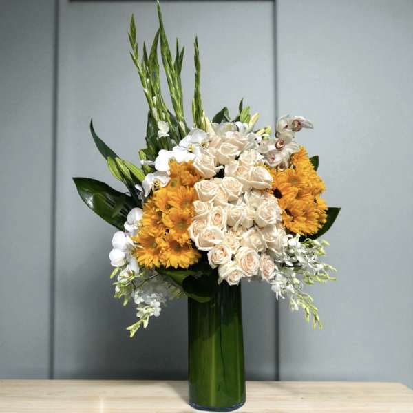 Tall bouquet of cream roses, white orchids, and orange flowers in a green glass vase