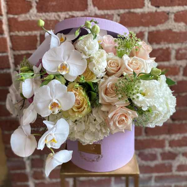 Bouquet of white orchids, pale roses, and hydrangeas in a lavender hat box