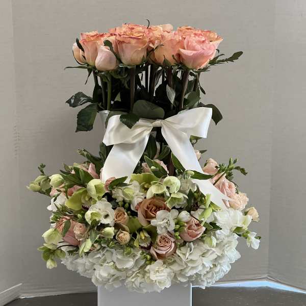 Tall floral arrangement of pink roses and white hydrangeas in a white vase with a ribbon