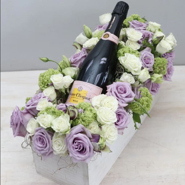 Lavender and white roses arranged around a champagne bottle in a white box