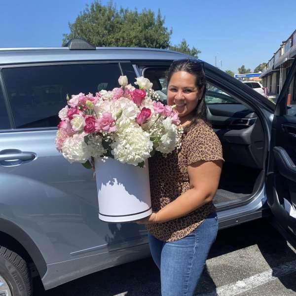 Woman holding a large pink and white flower arrangement in a white hatbox container