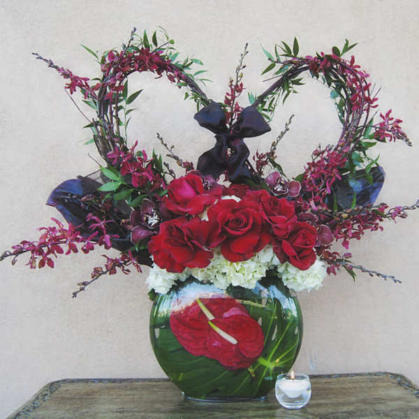 Heart-shaped floral arrangement with red roses in a glass vase
