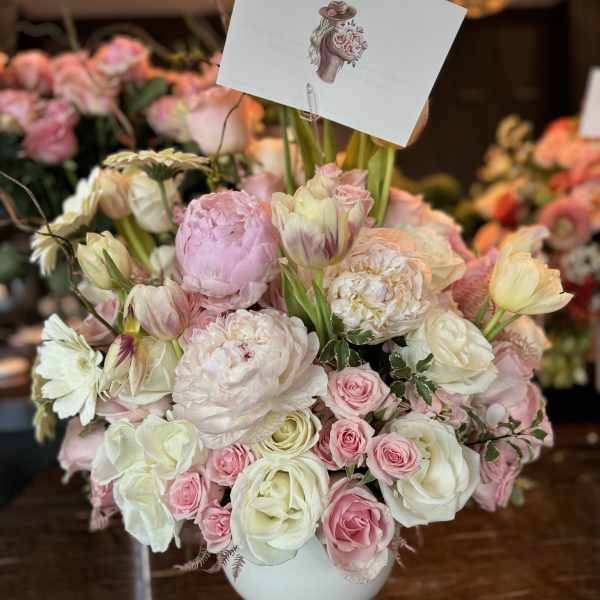 Pink and white bouquet in a white vase with a small card