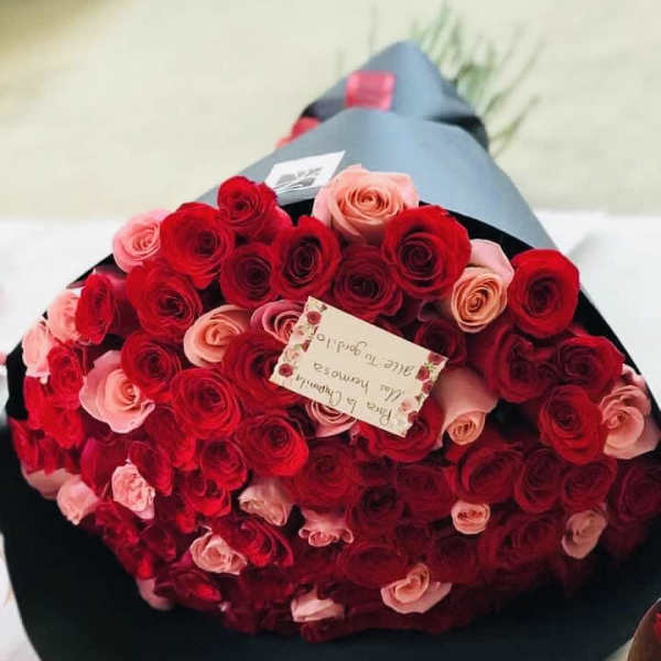Large bouquet of red and pink roses wrapped in black paper with a small card attached