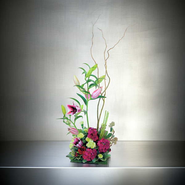 Tall floral arrangement with pink lilies and magenta blooms in a low container